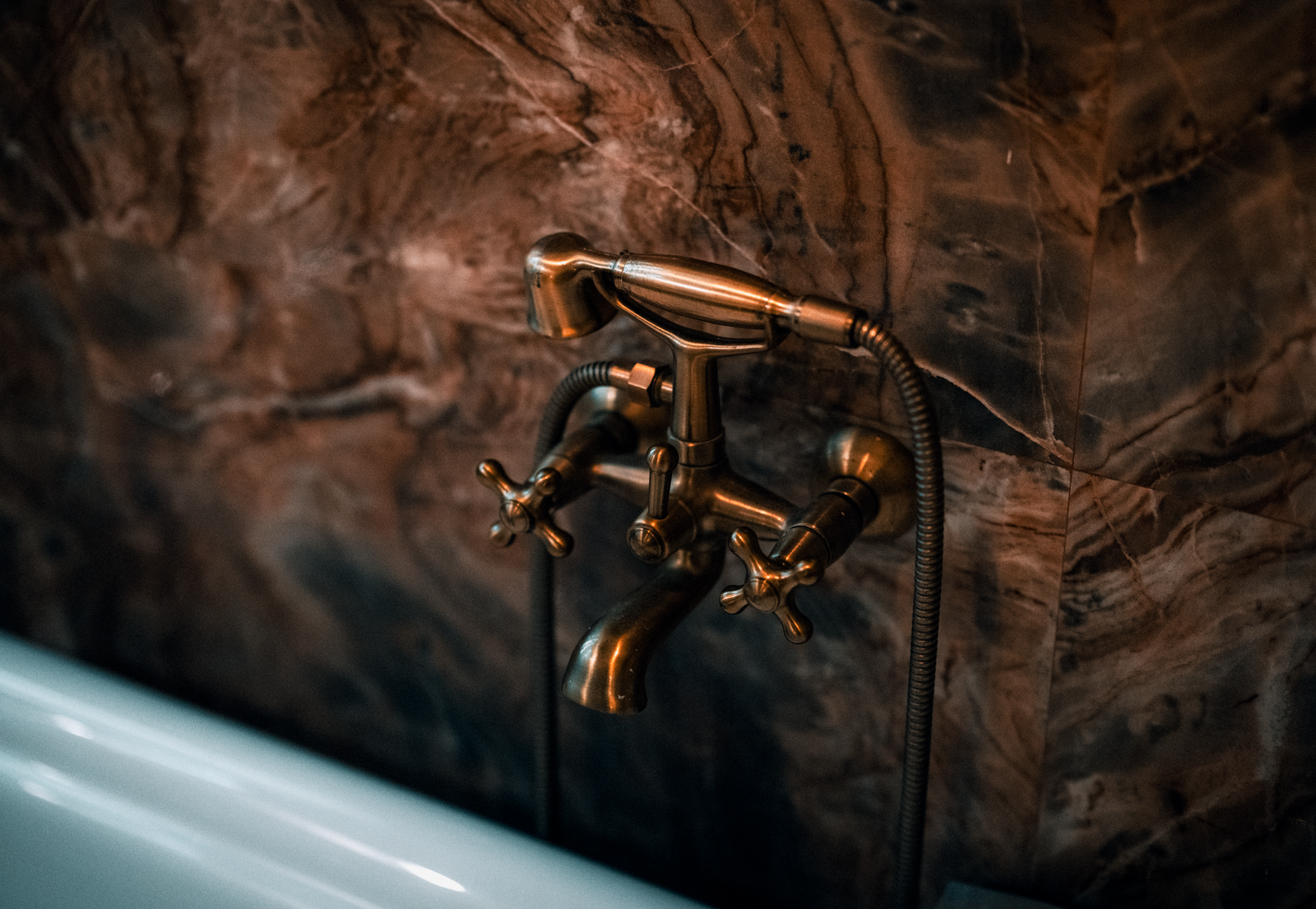 A brass bathroom faucet against a marble wall.
